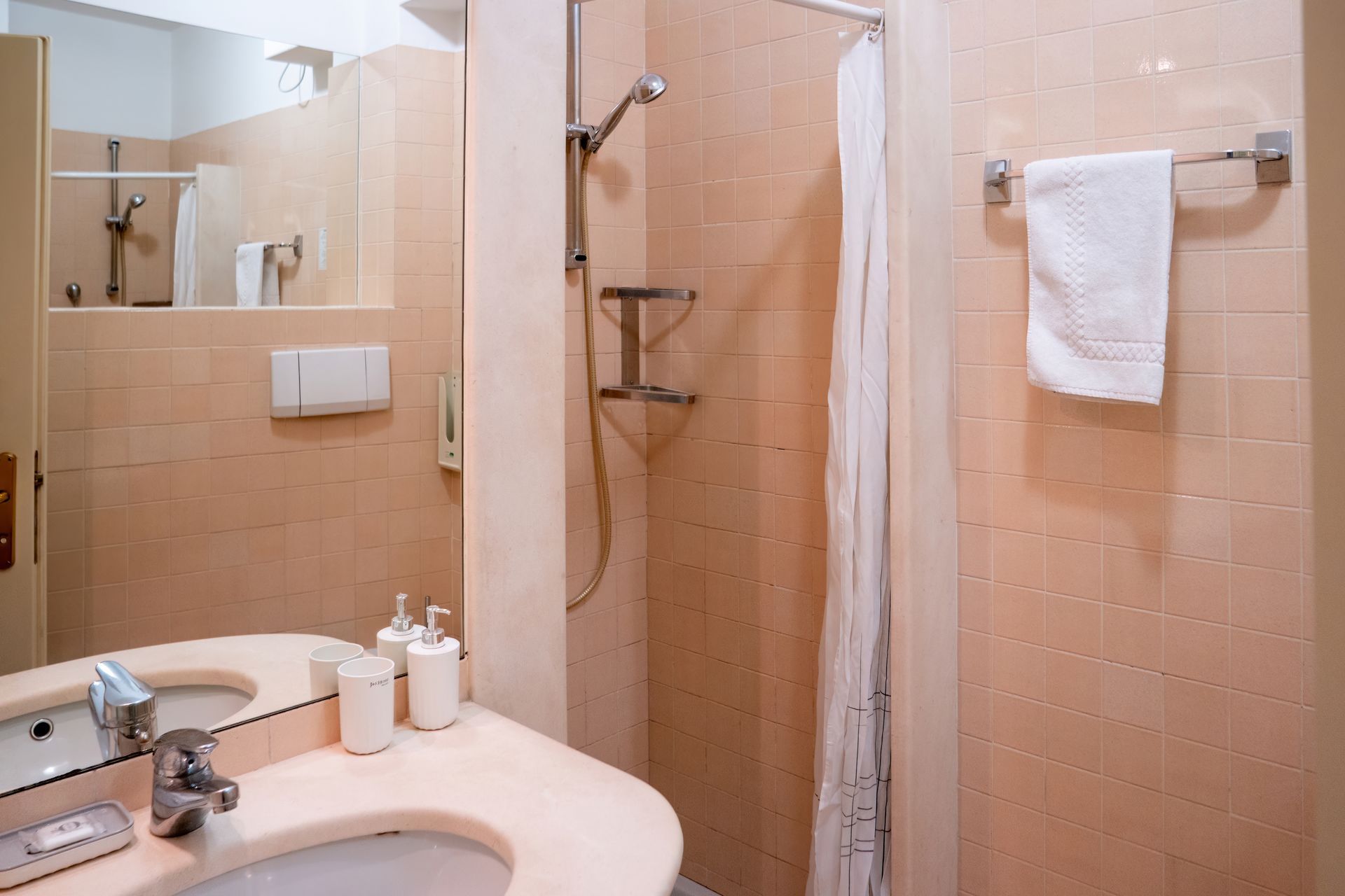 A small bathroom with a light-colored vanity, shower with a curtain, and a towel rack. The walls are tiled.