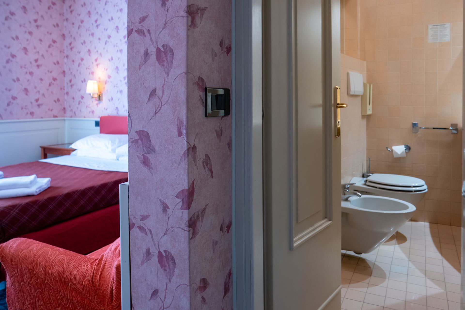 View through a doorway into a hotel room, showing a bed and a bathroom with a toilet and bidet.