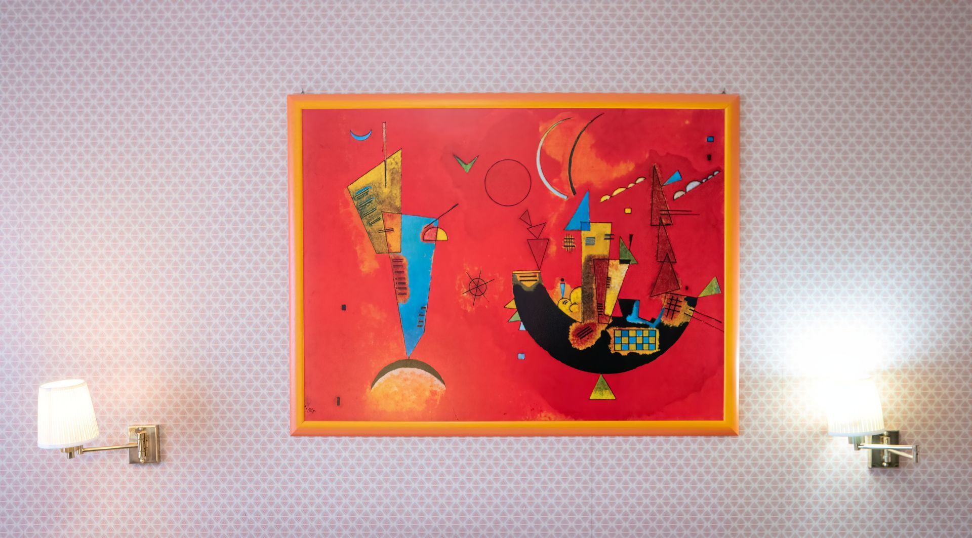 Abstract art piece with red background, blue shapes, and gold frame, flanked by two sconce lights on patterned wallpaper.