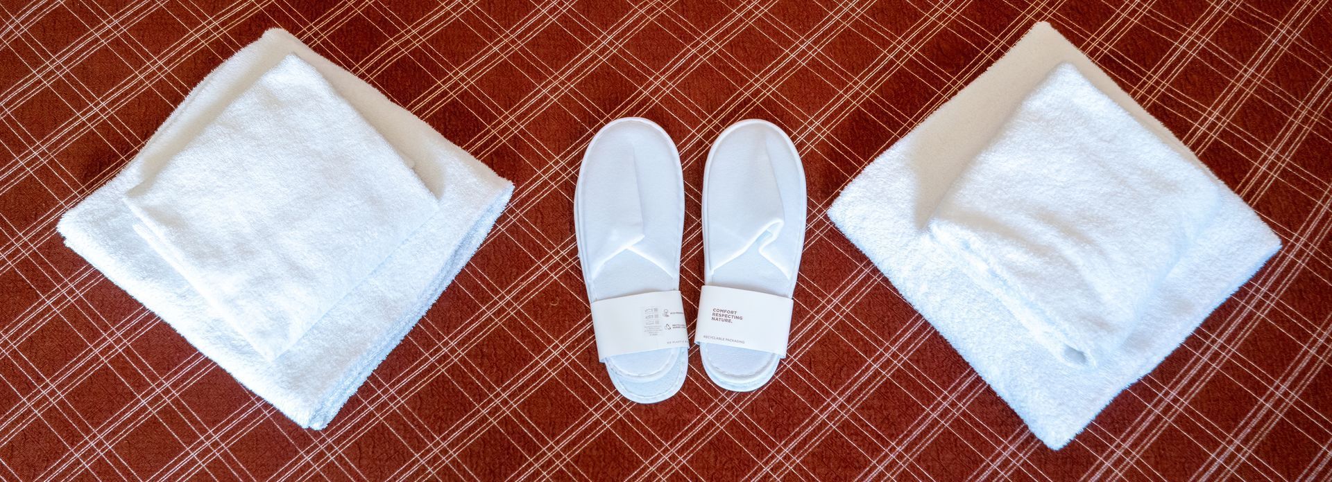 Folded white towels and disposable slippers arranged on a patterned, reddish-brown surface.