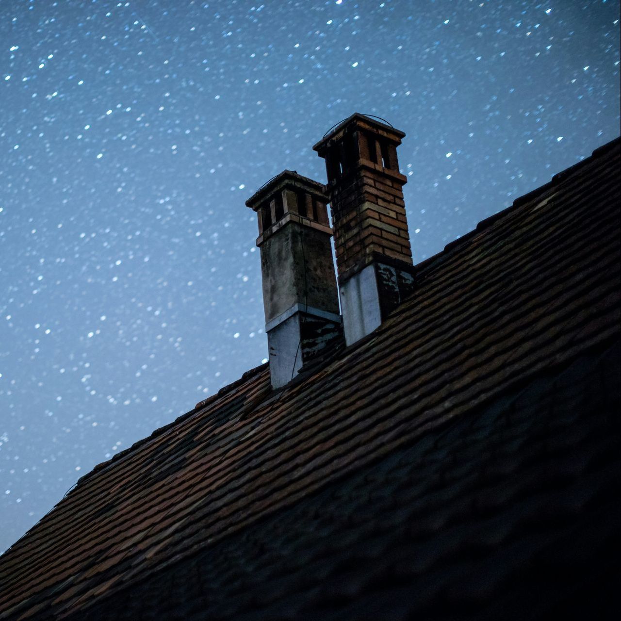 Two chimneys on the roof of a house under a starry night sky