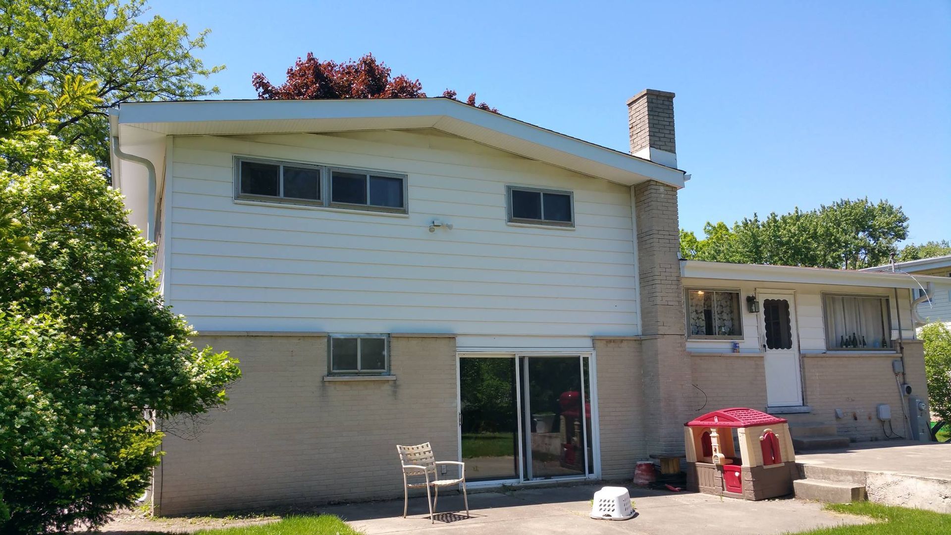 The back of a house with a sliding glass door and a playhouse in the backyard.