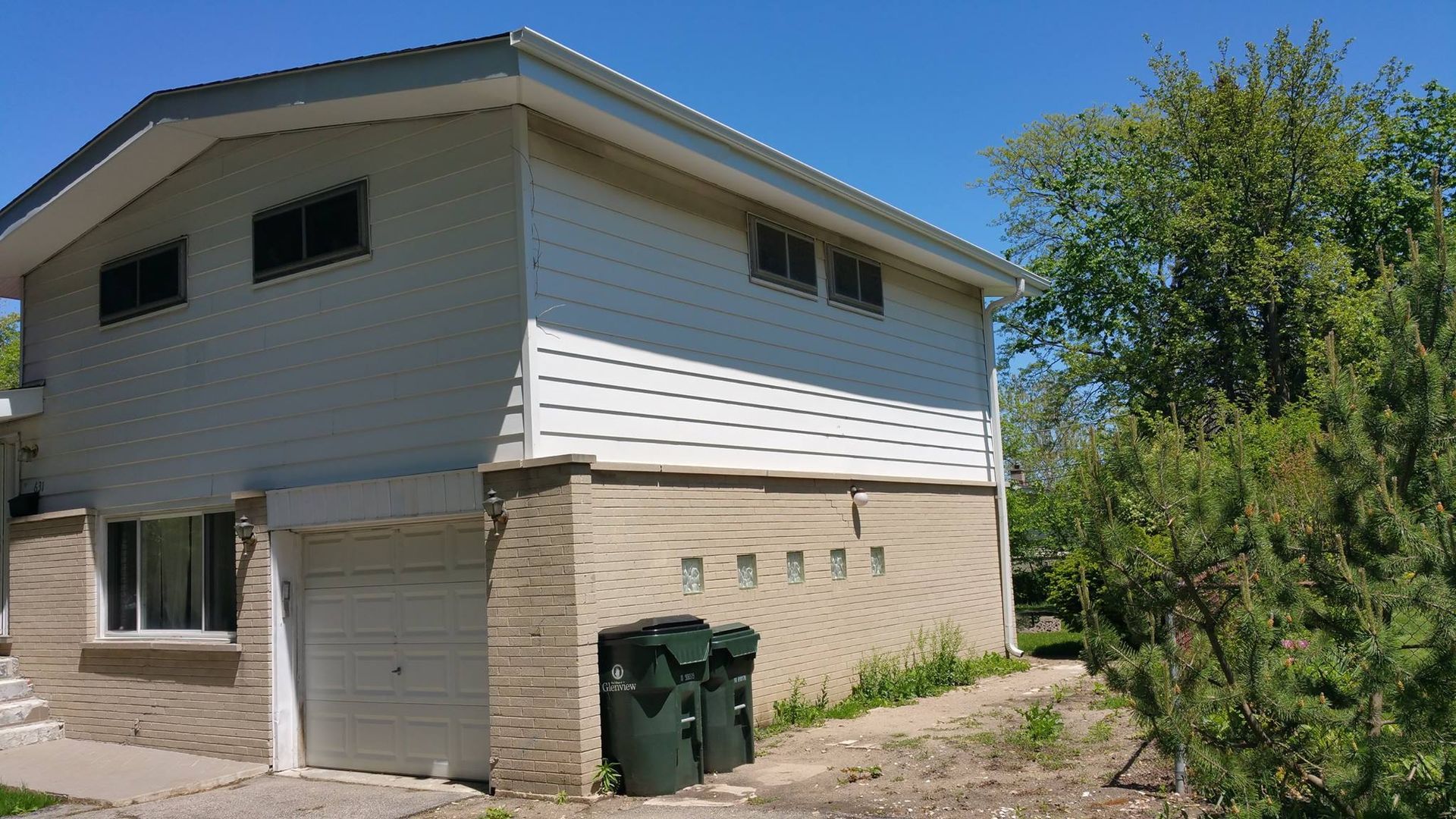 A house with a garage and trash cans in front of it