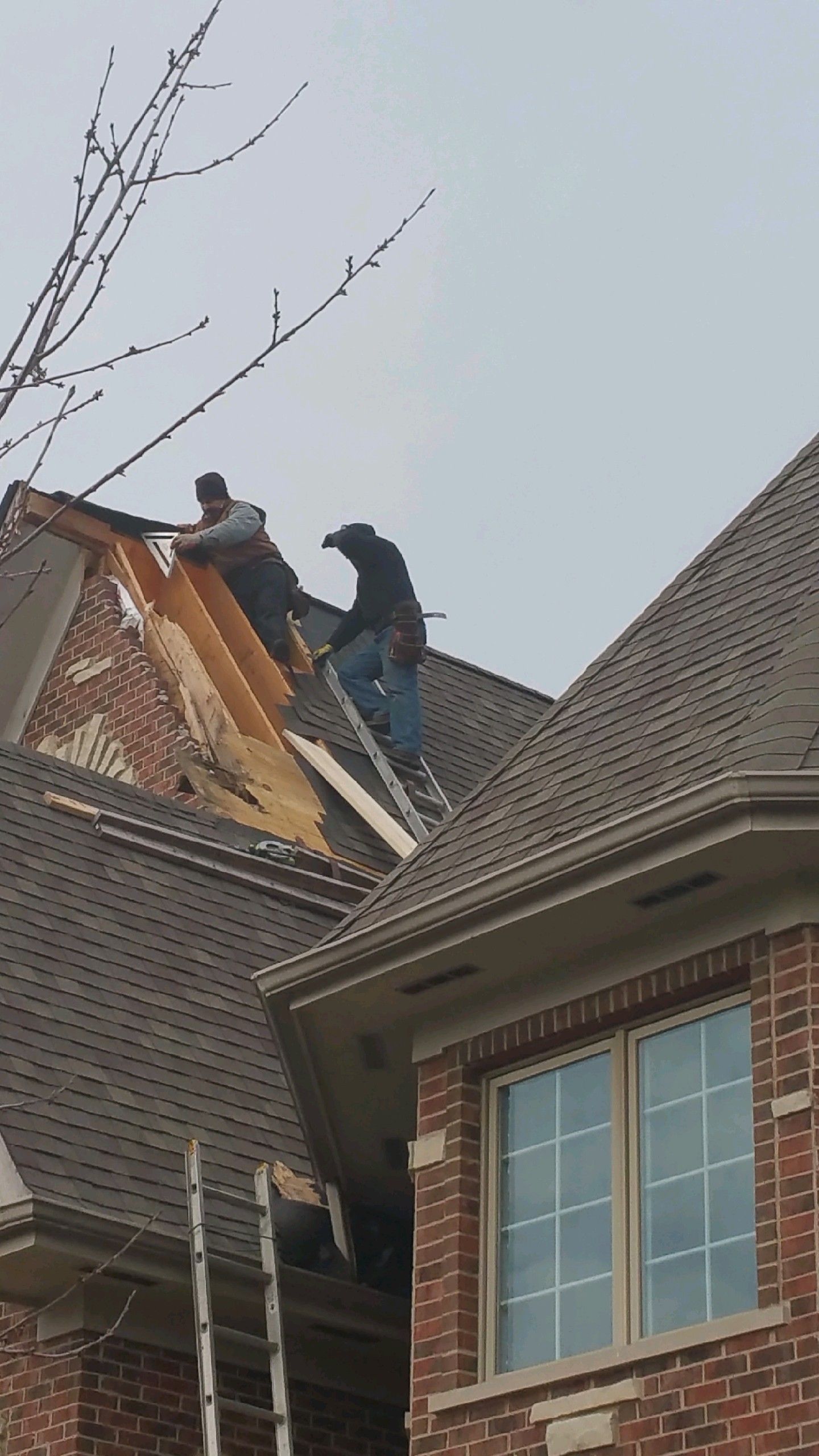 Two men are working on the roof of a brick house.
