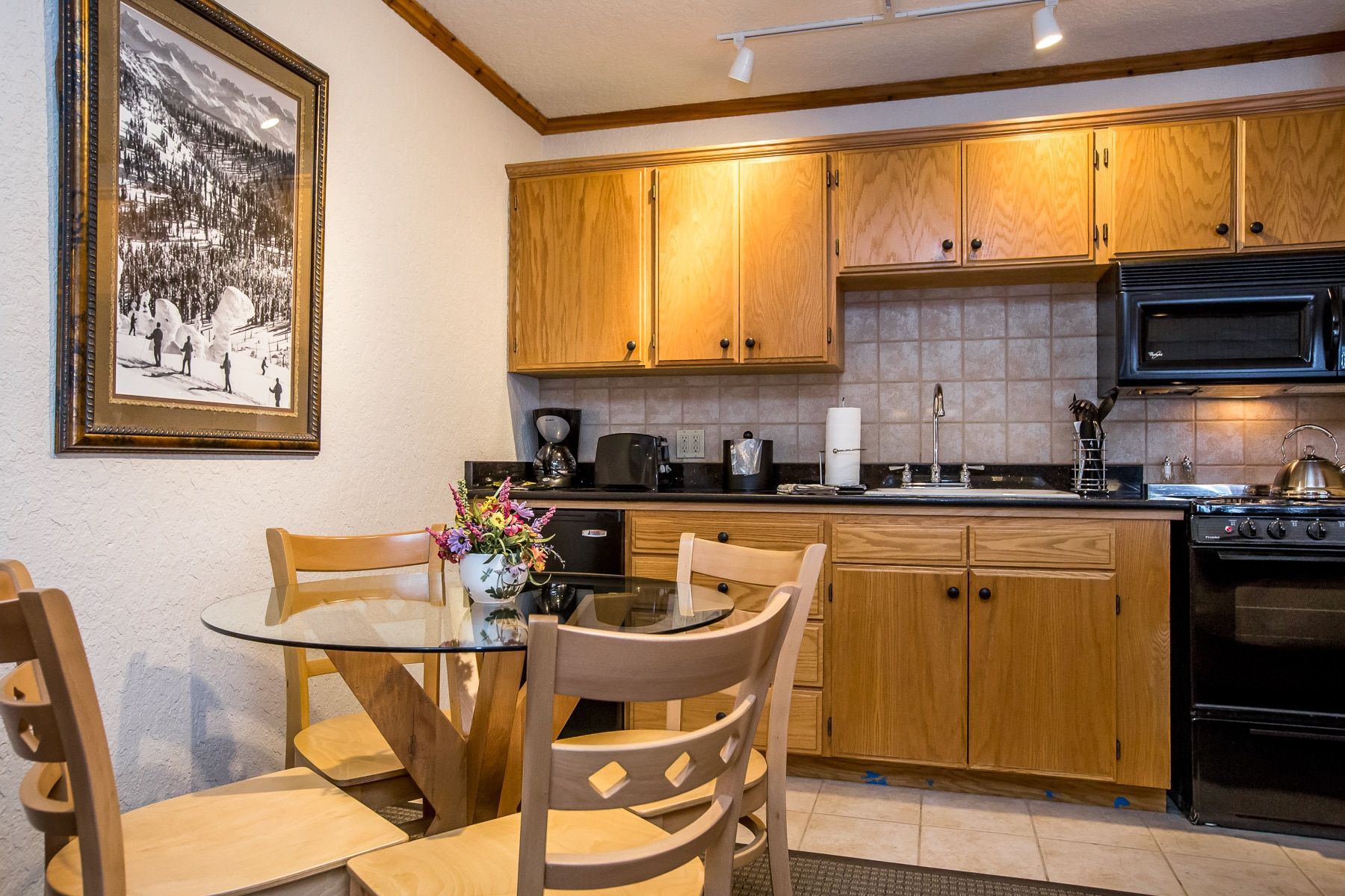 Kitchen with wooden cabinets, small table with chairs, and a microwave and stove.