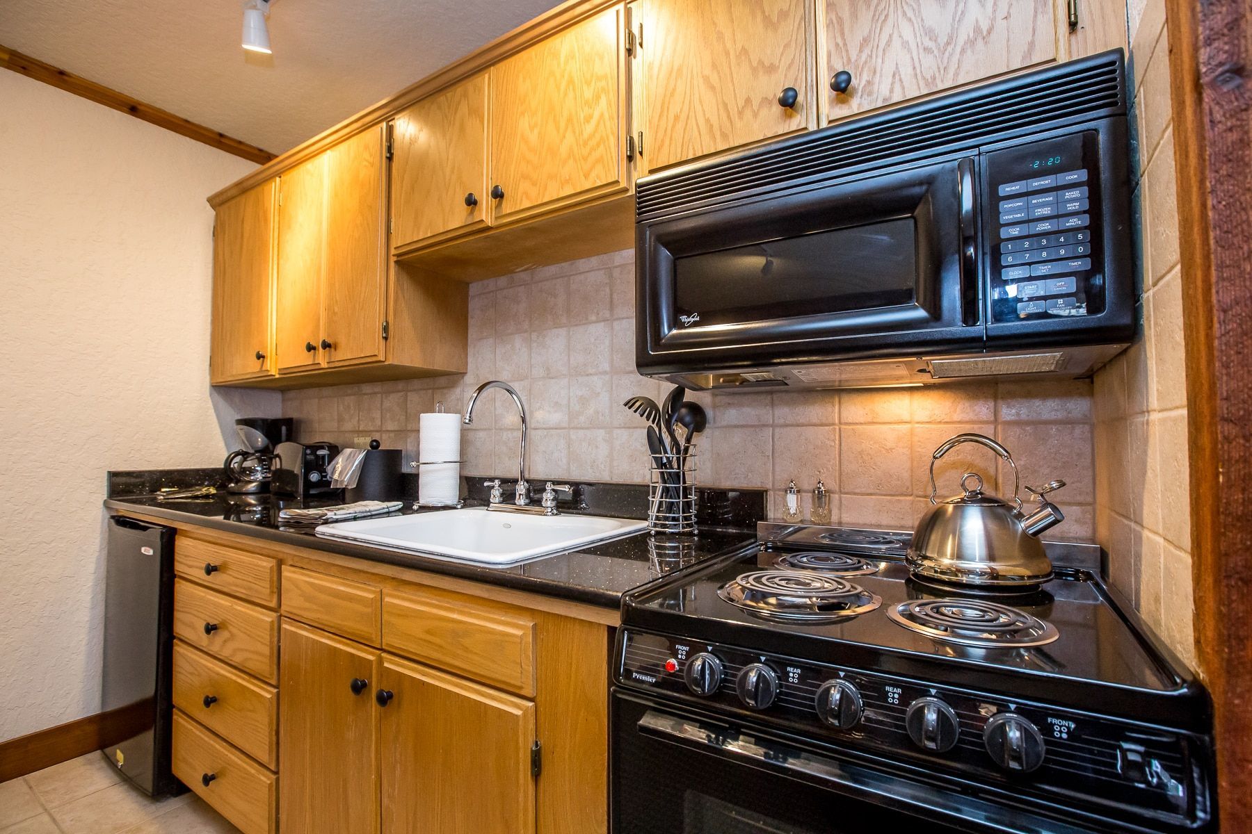 Kitchen with light wood cabinets, black countertops, and appliances.