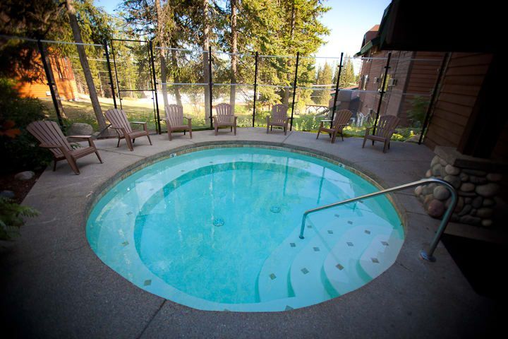 Outdoor hot tub with clear water, surrounded by Adirondack chairs, near a fence and trees.