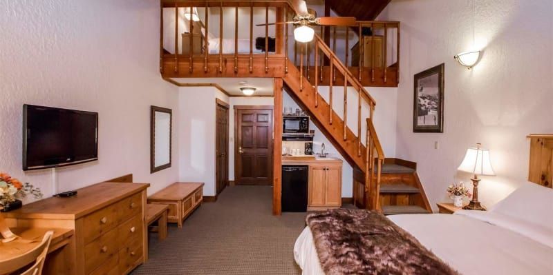 A hotel room with a bed , desk , television and stairs leading to the second floor.