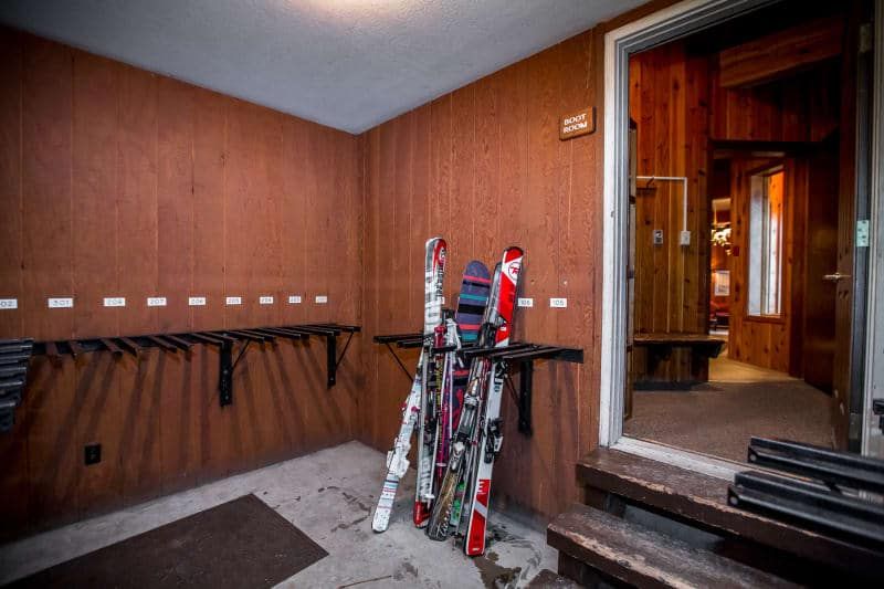 Ski storage room with skis and racks, brown wood paneling, and open doorway.