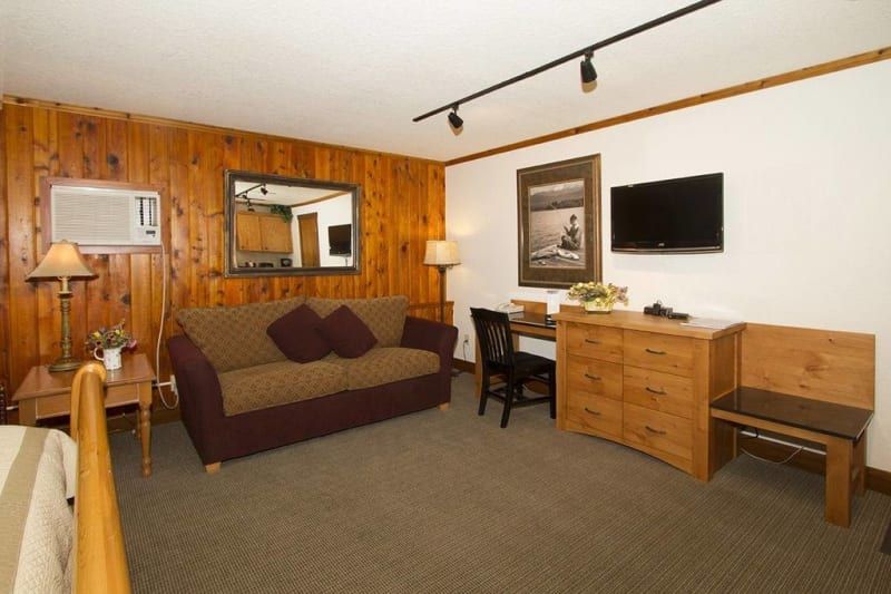 Cozy motel room with wood paneling, a sofa, TV, desk, and dresser.