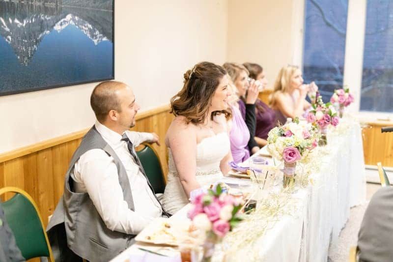 A bride and groom are sitting at a long table at a wedding reception.