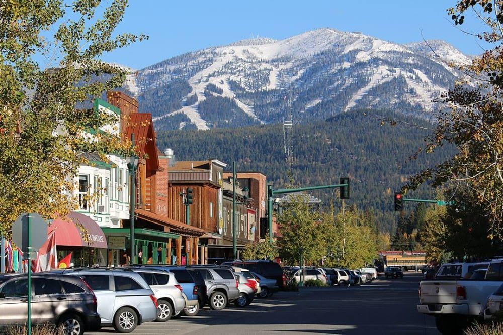 A city street with a mountain in the background and a lot of cars parked on the side of the road.