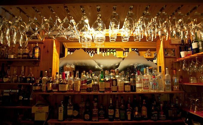 Bar with bottles, glasses hanging above, and a mountain-shaped mirror. Warm lighting illuminates the wood interior.