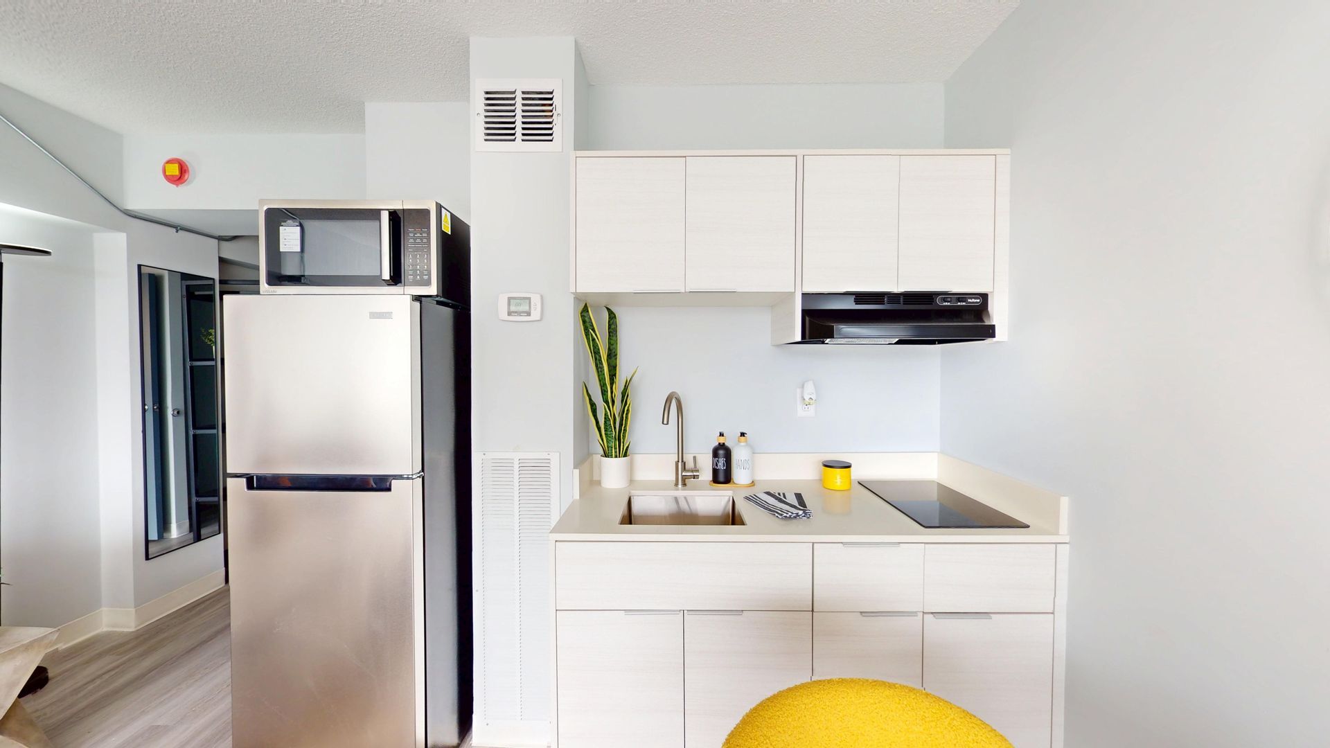 A small kitchen with white cabinets, stainless steel fridge, microwave, and a window.