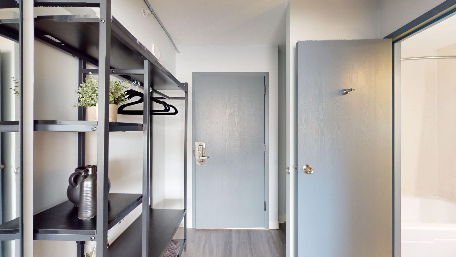Hallway with gray door, shelving unit, and another door on the right.