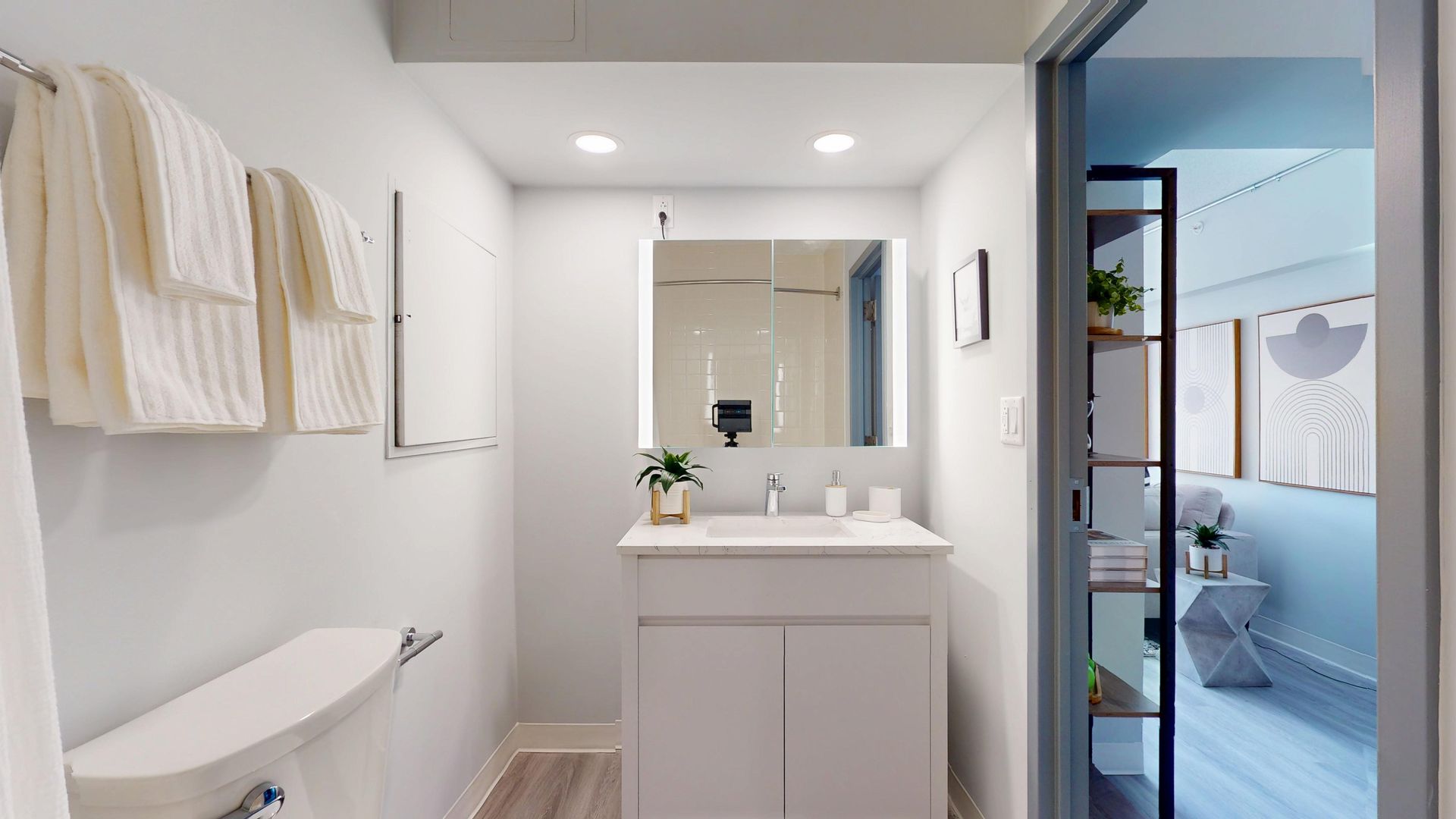 Modern white bathroom with white towels, vanity, and a view into a bedroom with art.