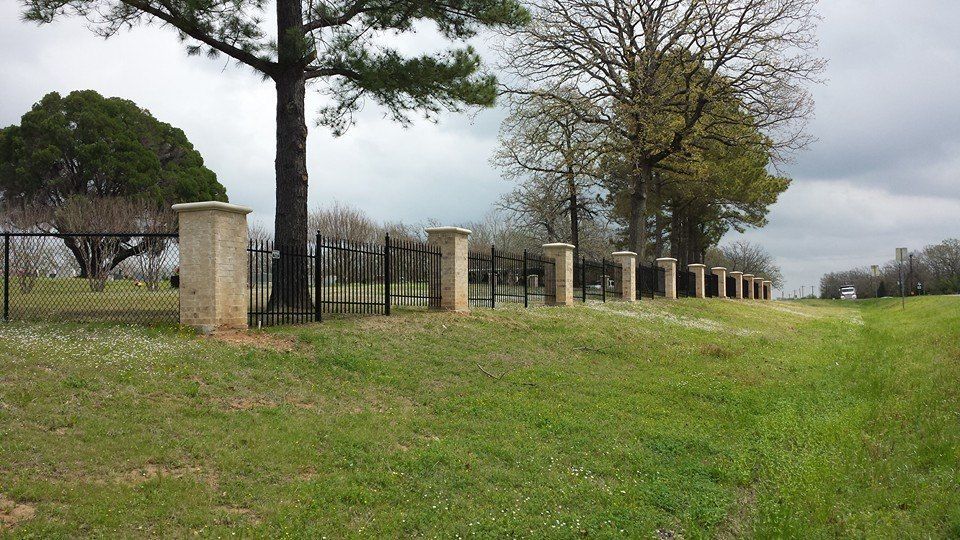 A fence surrounds a grassy field with trees in the background