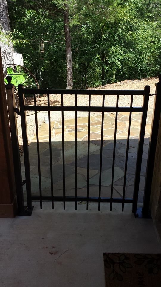 A black gate is open to a patio with trees in the background.