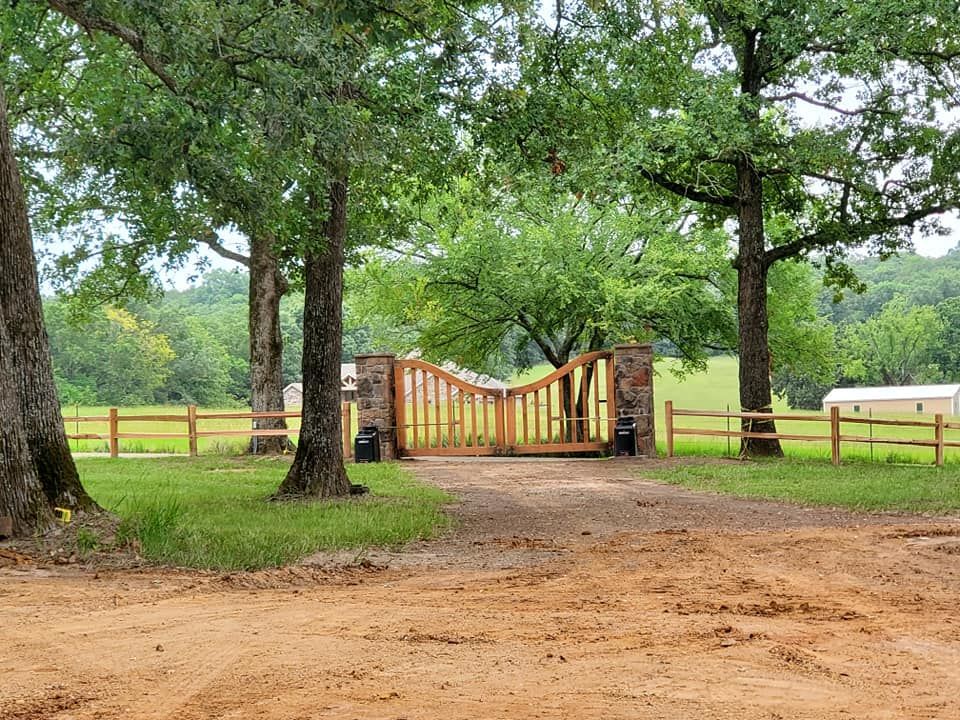 A wooden gate is surrounded by trees on a dirt road.