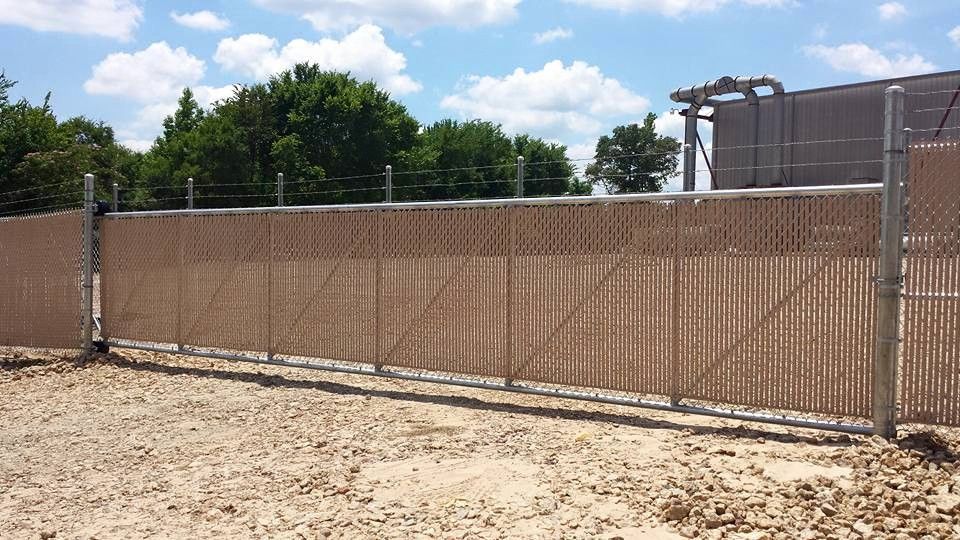 A chain link fence surrounds a dirt field with trees in the background