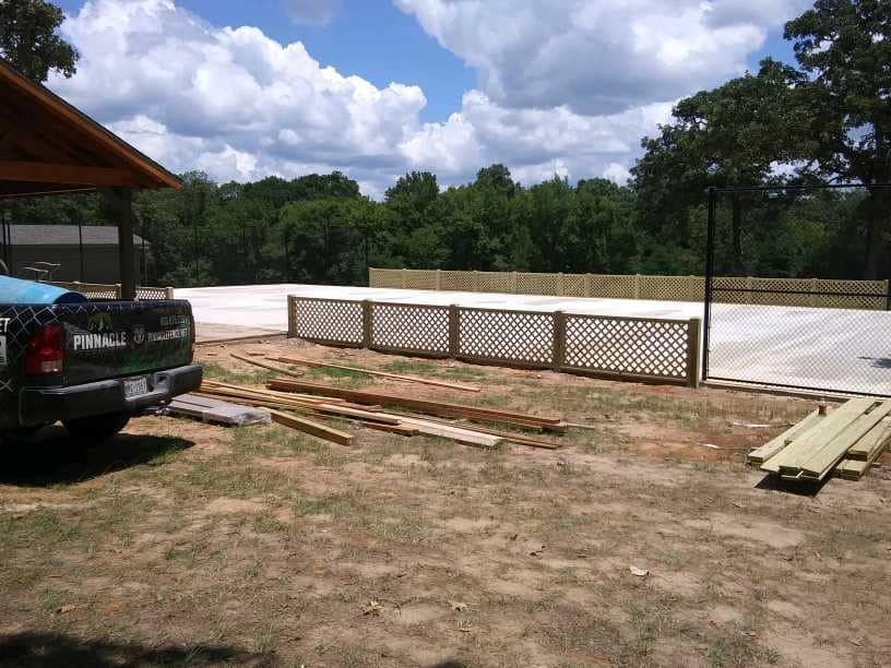 A pickup truck is parked in a dirt field next to a wooden fence.