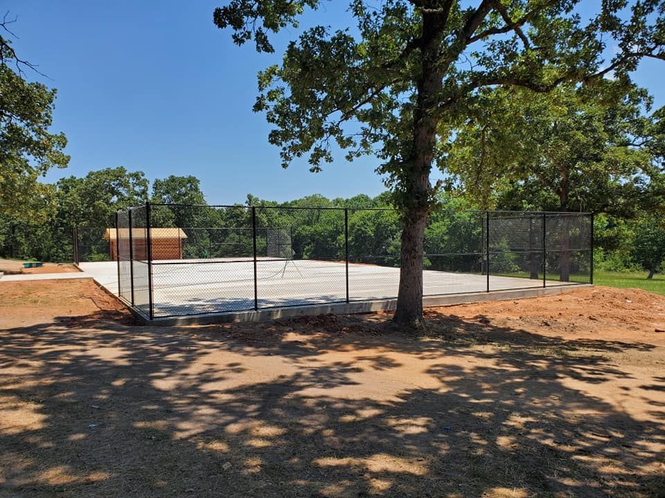 A basketball court with a fence around it and trees in the background.