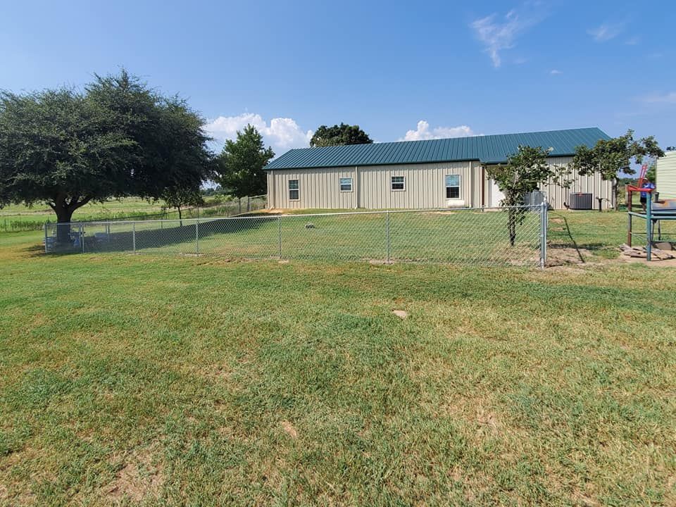 A house with a green roof sits in the middle of a grassy field