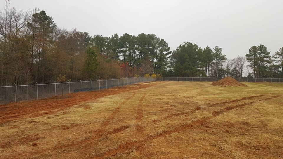 A large dirt field with a fence in the background and trees in the background.