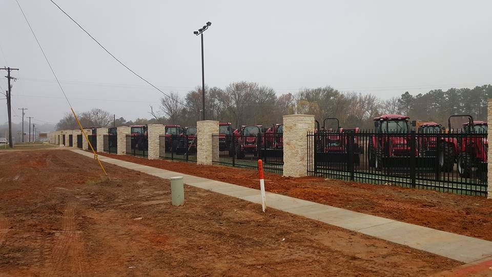 A row of tractors parked behind a fence next to a sidewalk.