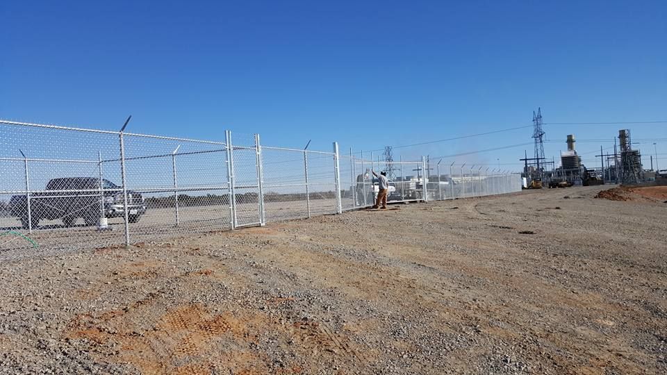 A chain link fence is surrounding a dirt field.