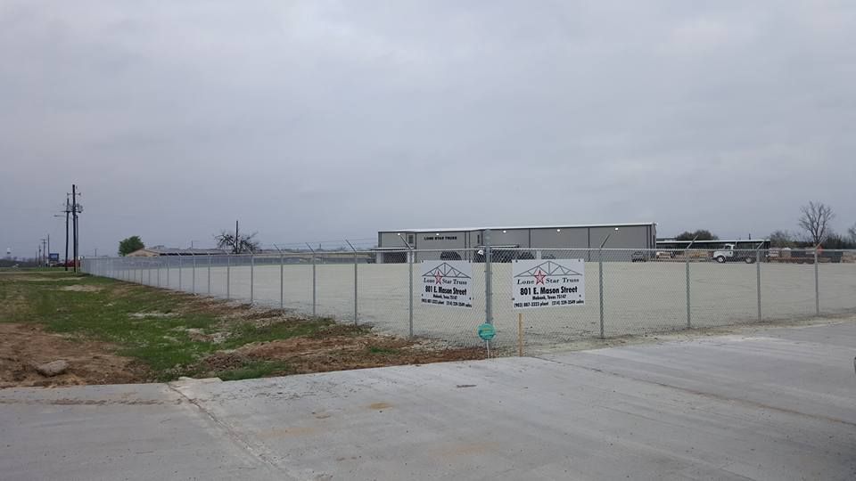 A fence surrounds a large empty lot with a building in the background.