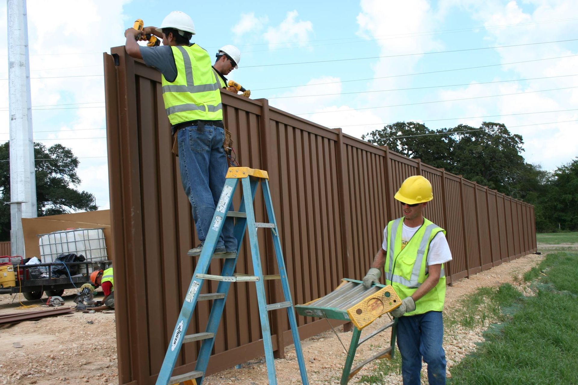 Two construction workers are working on a wooden fence.