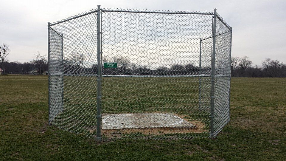A chain link fence surrounds a base in a baseball field.