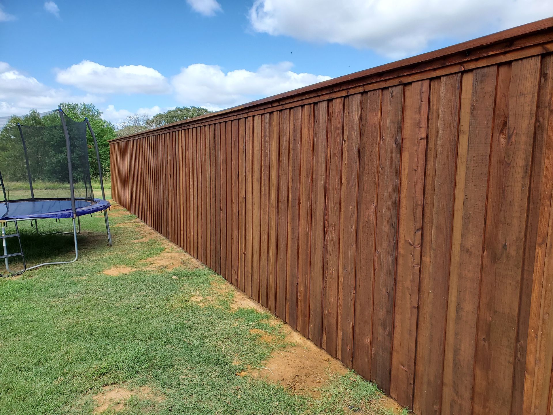 A wooden fence with a trampoline in the backyard.