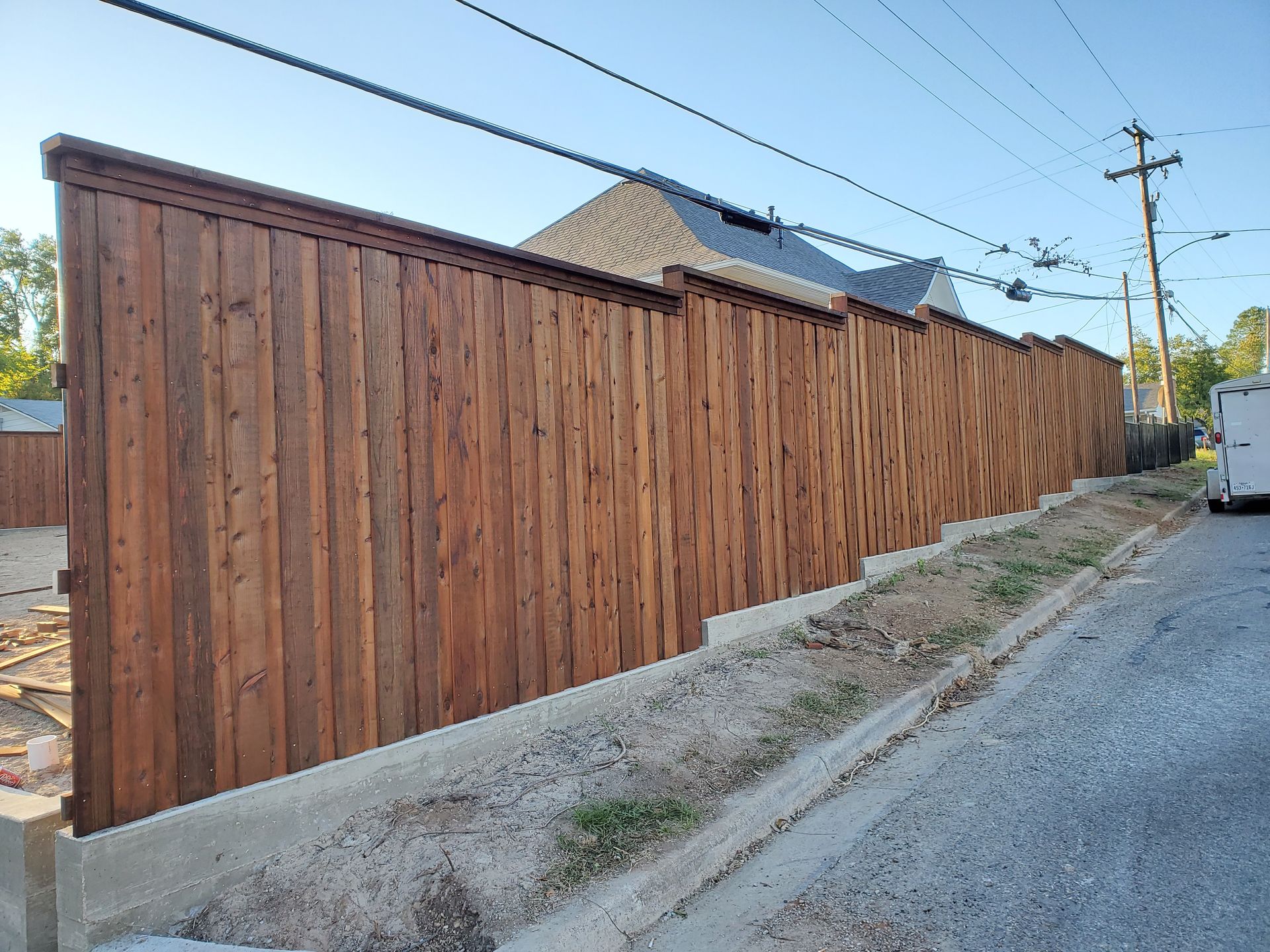 A wooden fence is sitting on the side of a road next to a house.