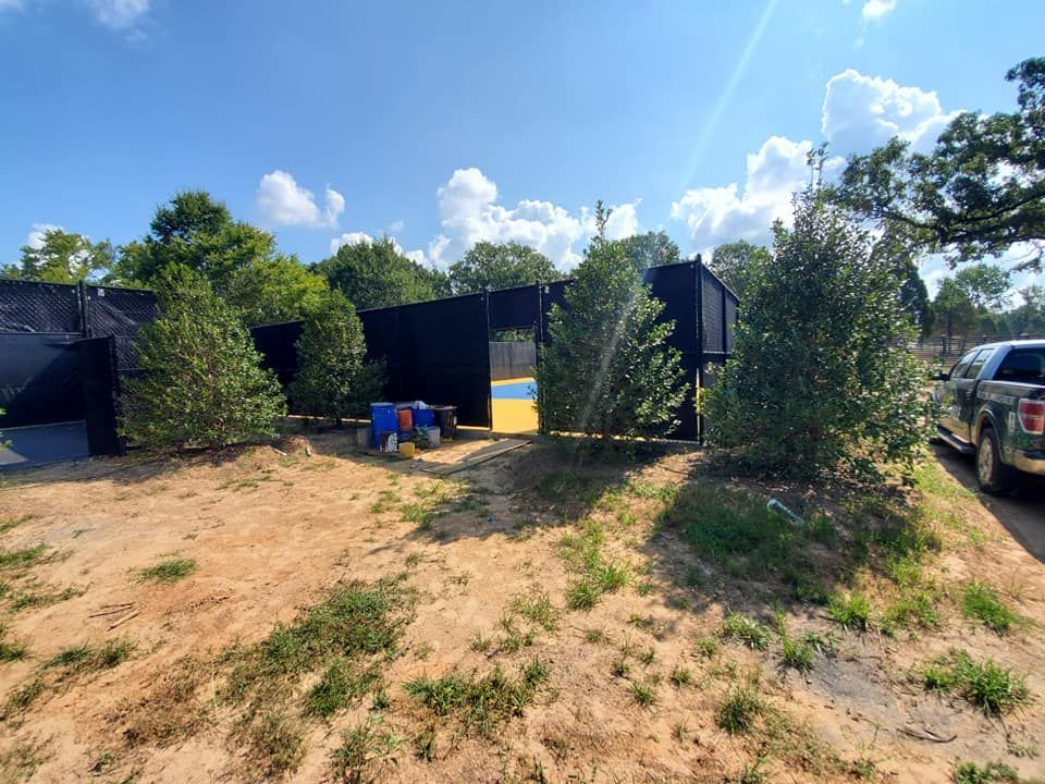 A black truck is parked in a dirt field next to a fence.