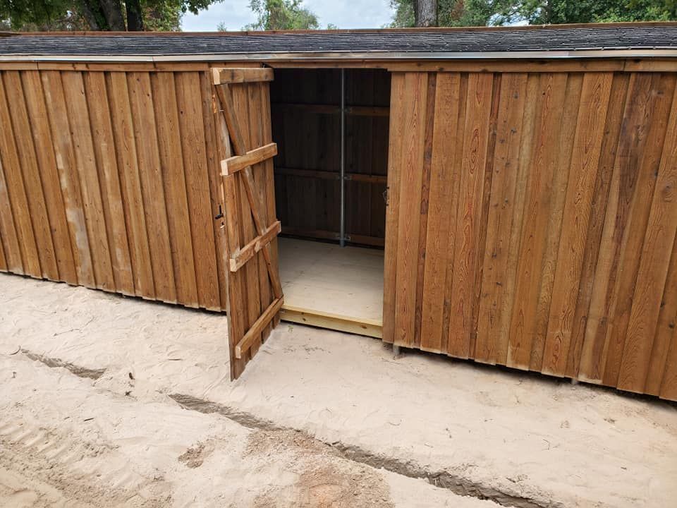 A wooden shed with the door open and a roof.