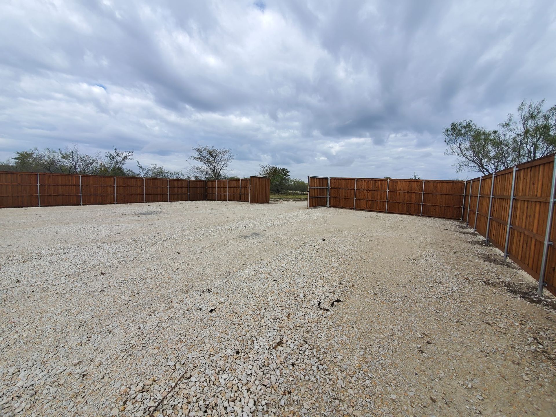 A gravel area with a wooden fence and a cloudy sky in the background.