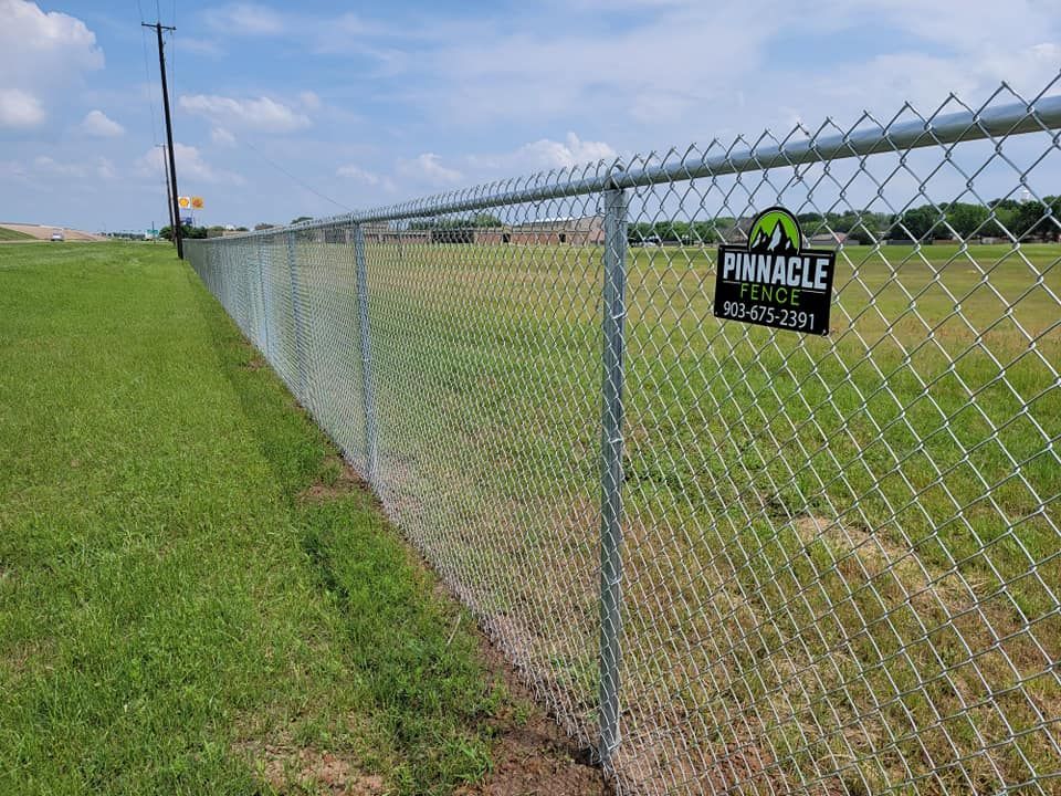 A chain link fence is surrounding a grassy field.