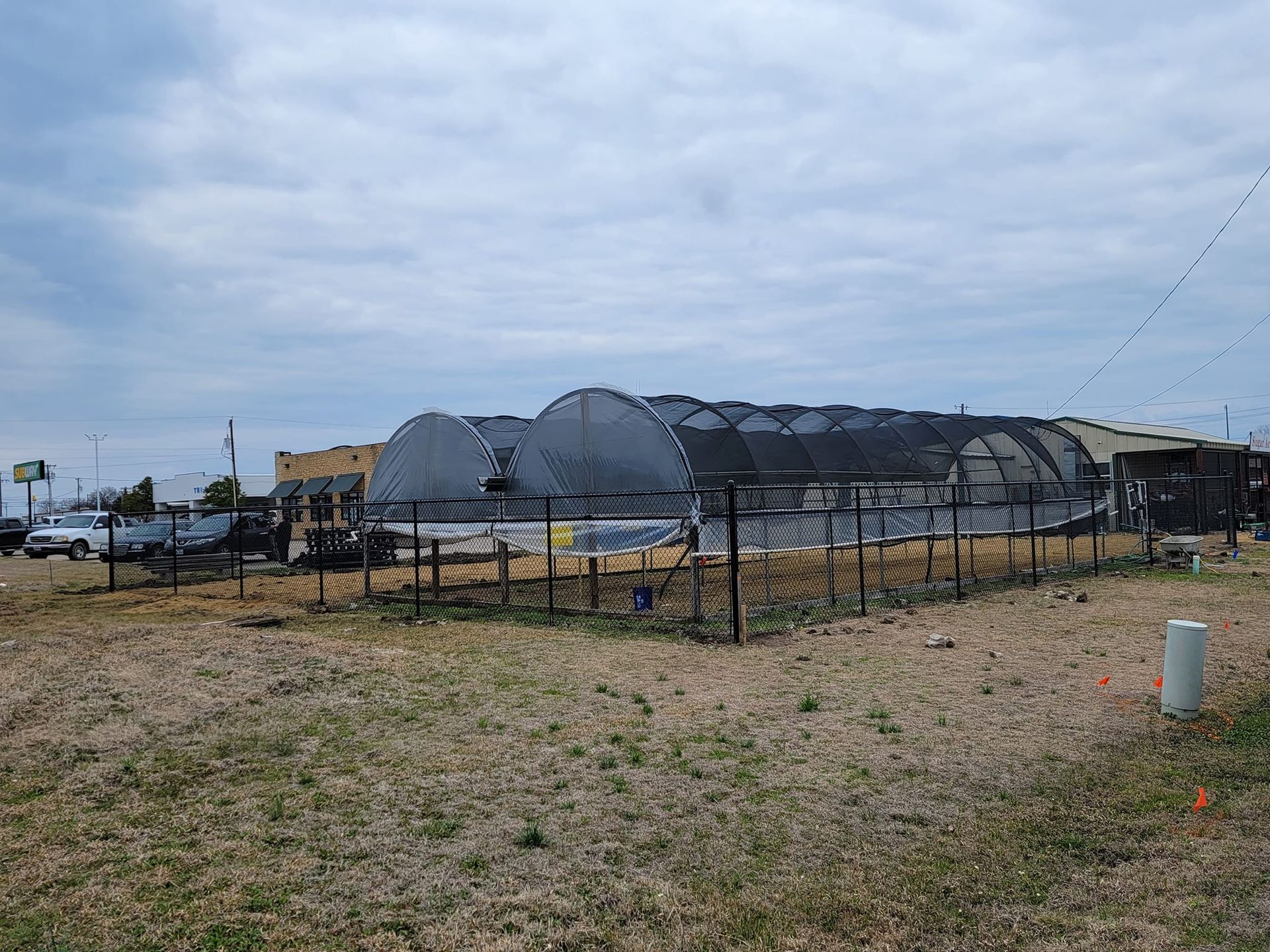 A group of greenhouses are sitting in a field behind a fence.