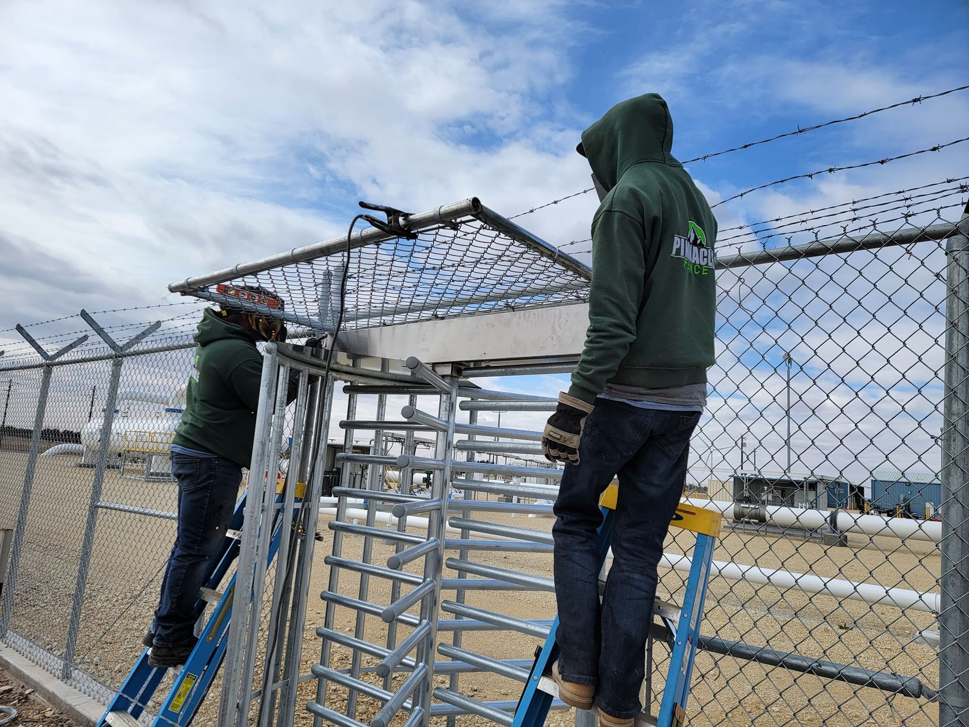 A man is standing on a ladder next to a chain link fence.