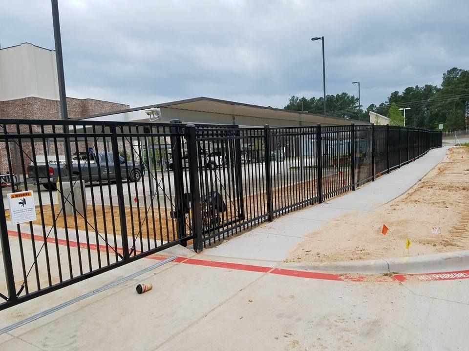 A black metal fence surrounds a concrete sidewalk in front of a building.