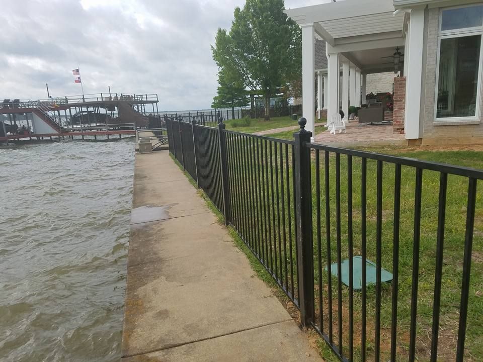 A fence along a sidewalk leading to a house next to a body of water.