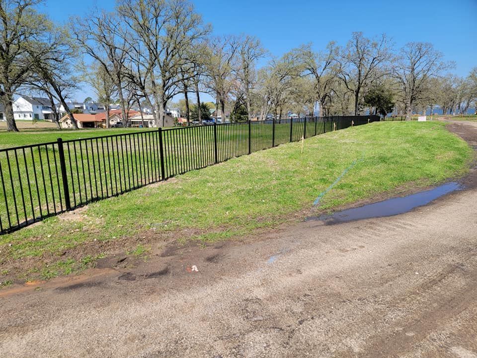 A black fence surrounds a grassy field next to a dirt road.