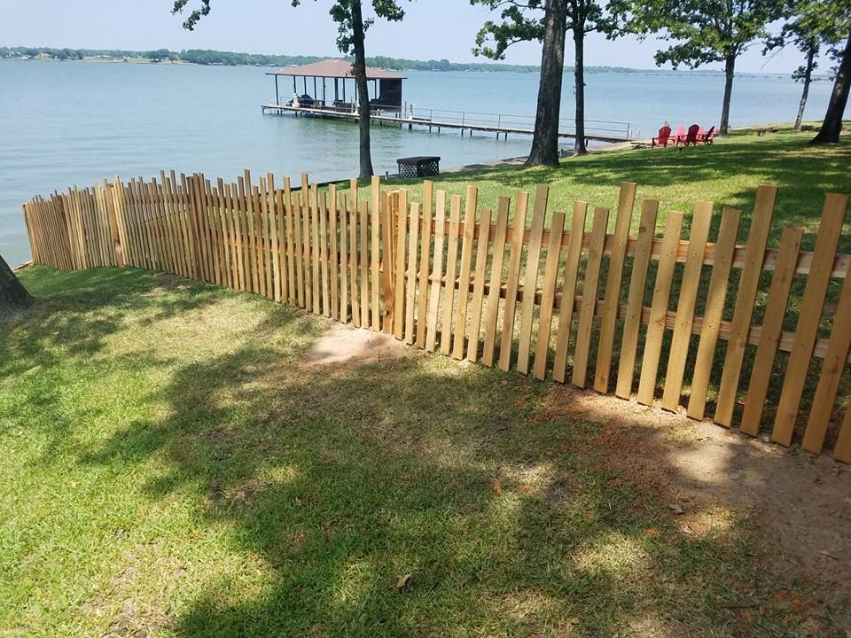 A wooden fence surrounds a lake with a dock in the background.