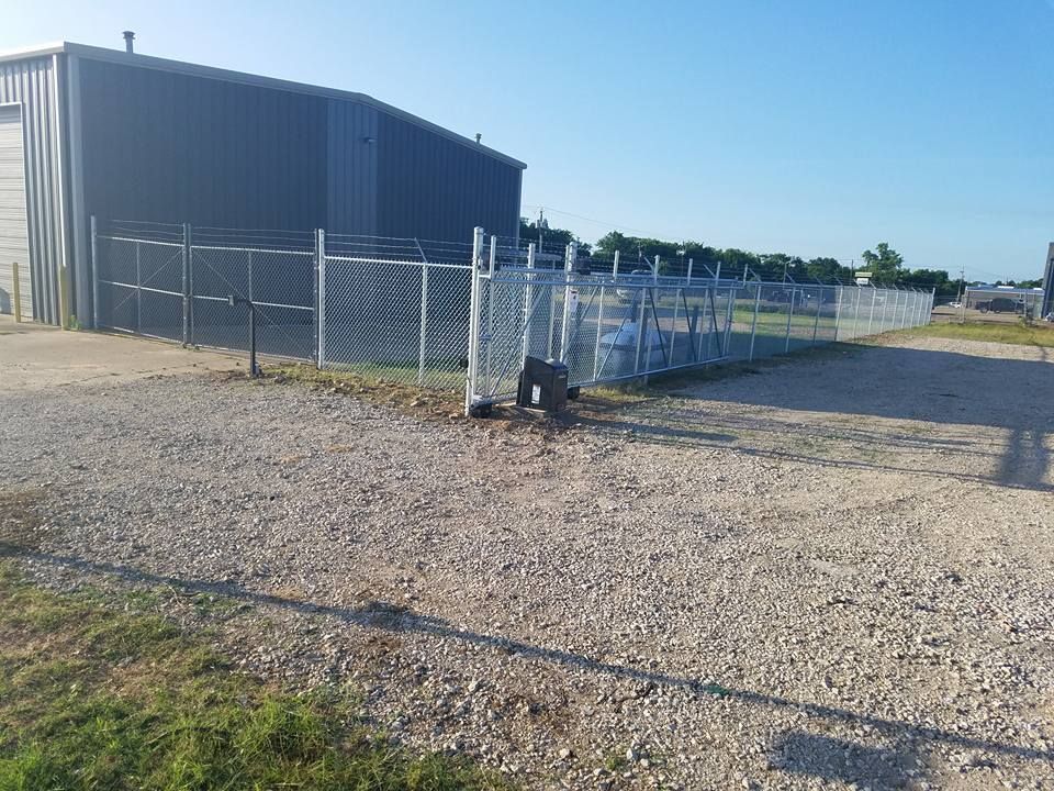 A chain link fence surrounds a gravel road in front of a building.