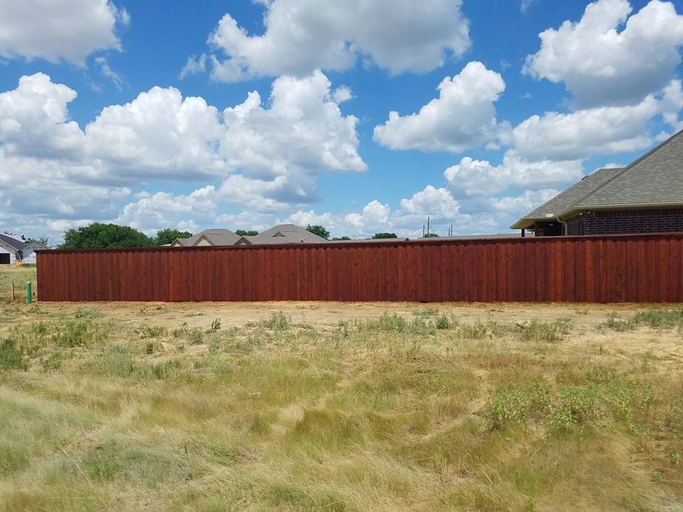 A red fence surrounds a grassy field in front of a house.