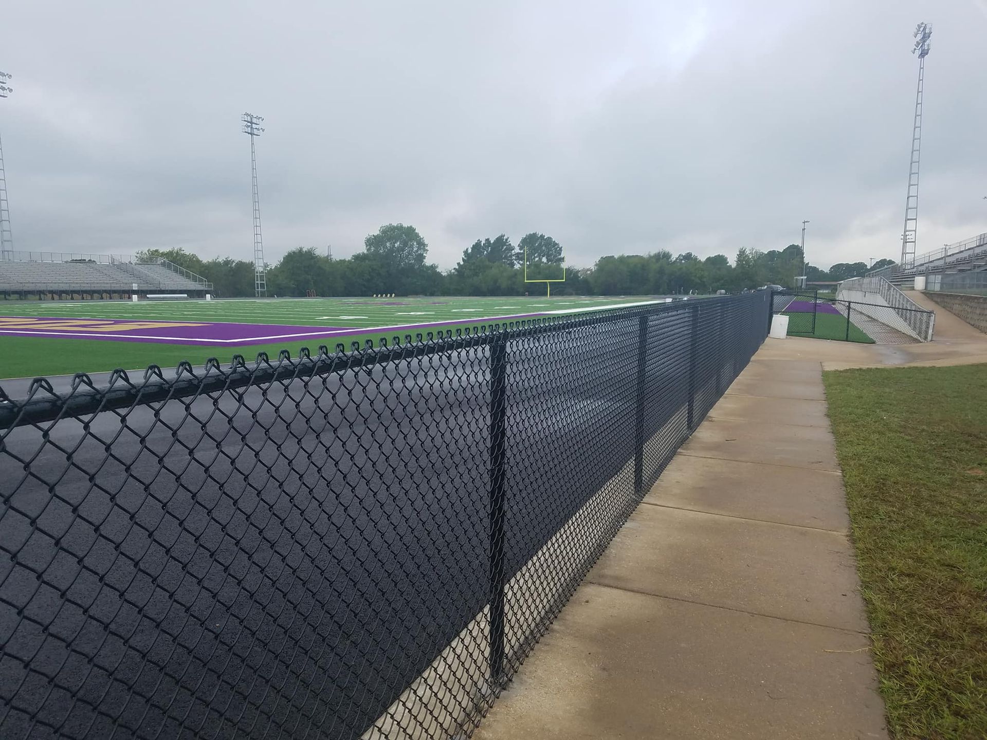 A chain link fence surrounds a football field on a cloudy day.