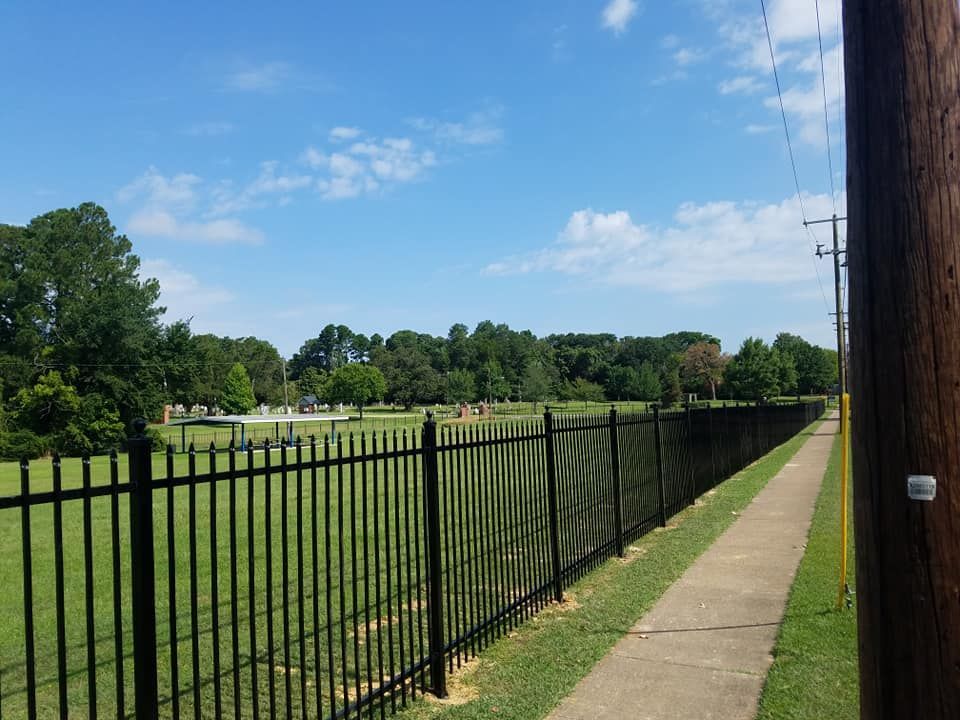 A black fence along a sidewalk leading to a field.
