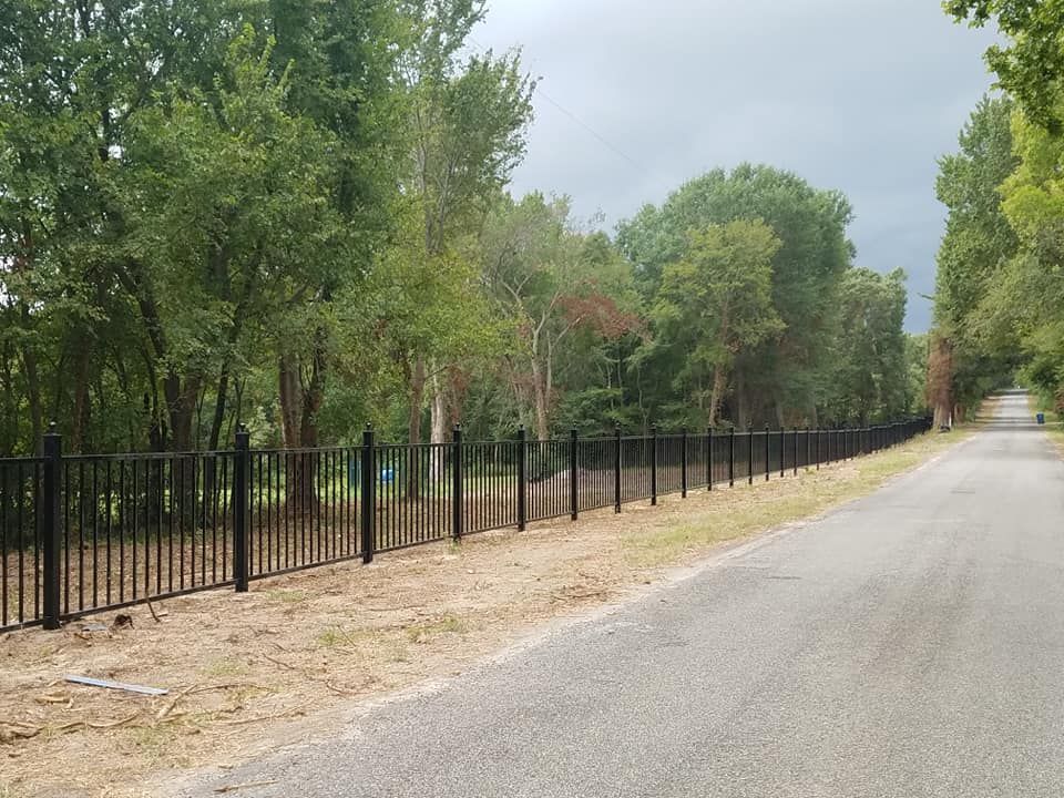 A black fence along the side of a road surrounded by trees.